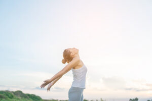 Young beautiful woman raising hands with beautiful view at meado