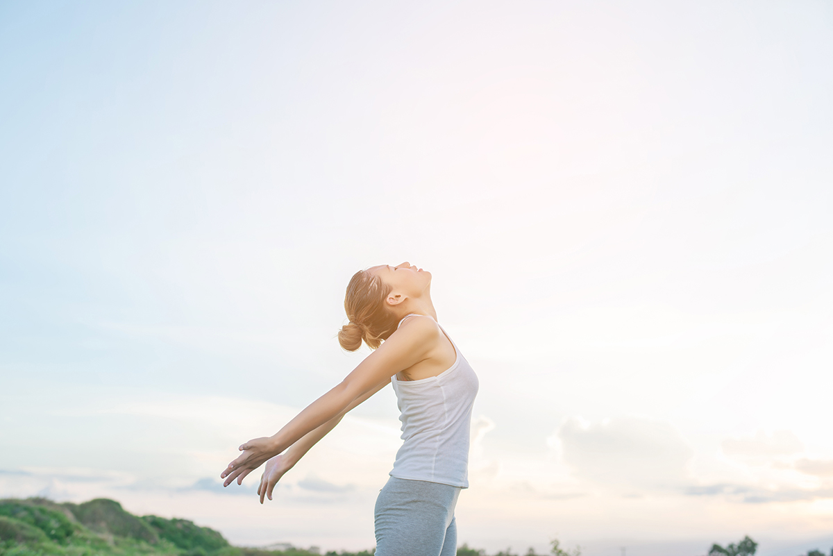 Young beautiful woman raising hands with beautiful view at meado